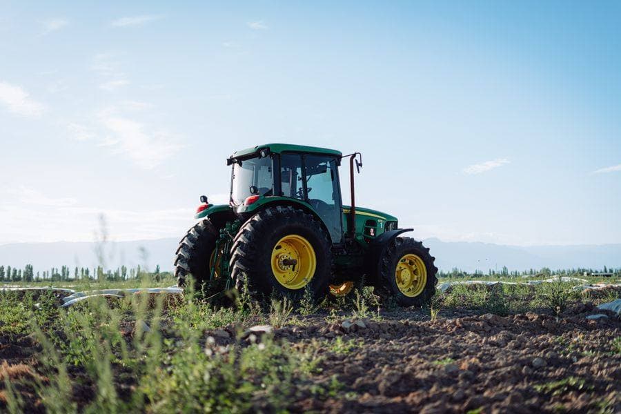 Зелений колісний трактор John Deere на зораному полі